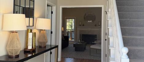 A spacious living area with a staircase, a console table with lamps, a patterned rug, and a view into the dining area.