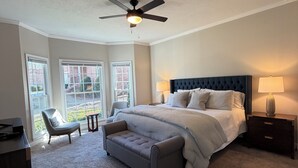 A bedroom with a large bed, a ceiling fan, a nightstand, a chair, and a view of the outside through large windows. - Abbeys at  WestLake , Wonderful 3-bedroom house with AC in charming Martinez. (Martinez)