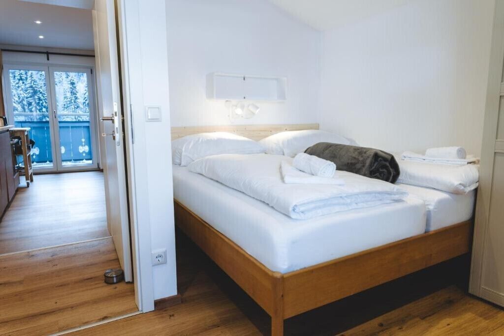 Een slaapkamer met een houten bed, wit beddengoed, een klein nachtkastje en uitzicht door een glazen deur op een balkon.