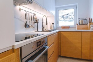 A modern kitchen with white cabinets, wooden accents, and a window providing a view of the outside. - Alpen Haus Maria/Two-room apartment (Viehhofen)