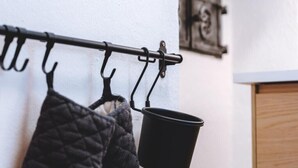 Ein schwarzer Metallhaken mit Haken, ein schwarzer Topf, der an einem der Haken hängt, und ein gestepptes Textil darunter.