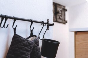 A black metal rack with hooks, a black pot hanging from one of the hooks, and a quilted fabric item hanging below. - Alpen Haus Maria/Two-room apartment (Viehhofen)