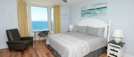 A bedroom with a bed, a chair, a nightstand, a ceiling fan, and a window with curtains.