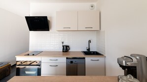A modern kitchen with a built-in oven, dishwasher, coffee maker, and a coffee grinder.