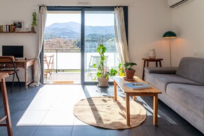 Ein modernes Wohnzimmer mit einer Couch, einem Holztisch, einem Fernseher und einem Balkon mit Bergblick.