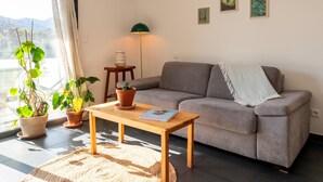 A living room with a sofa, a wooden table, potted plants, a lamp, and framed pictures on the wall.
