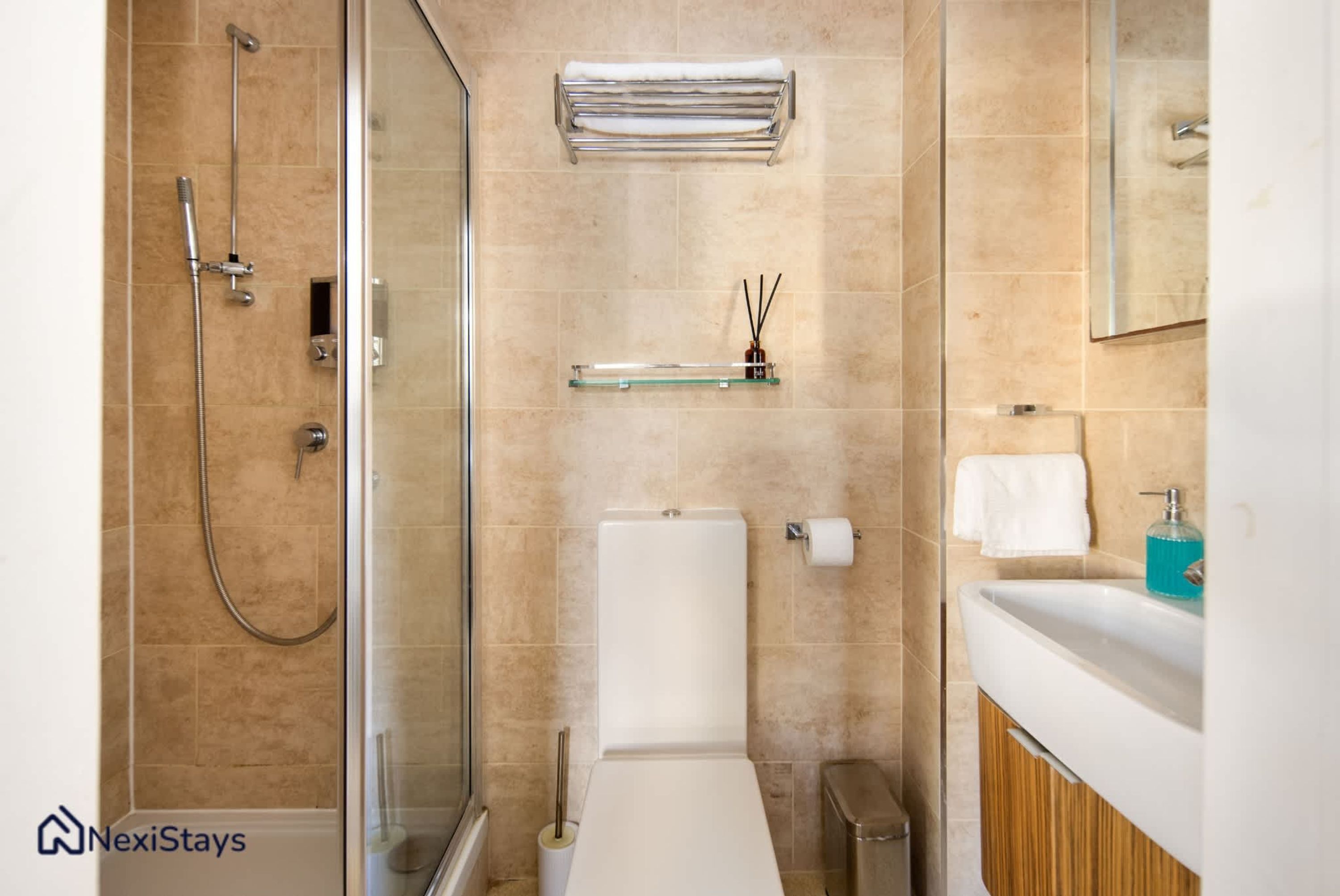 Un baño moderno con cabina de ducha de vidrio, inodoro, lavabo con espejo y un perchero para toallas.