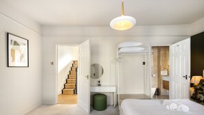 A bedroom with a bed, a bedside table, a mirror, a green waste bin, and a staircase leading to another room. - 10 Mins Walk to The Oval The Kennington Retreat (London)