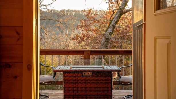 Um deck de madeira com mesa e cadeiras, com vista para uma área arborizada.
