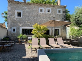 Un edificio de piedra con piscina, mobiliario exterior y una pérgola.