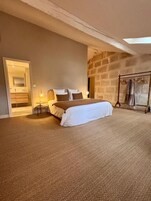 Un dormitorio amplio con una cama grande, una pared de piedra, un armario de madera y un baño visible a través de una puerta abierta.