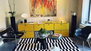 Een moderne woonkamer met een zwart-wit gestreept tapijt, een geel kastje, een zwarte stoel en een groot abstract schilderij aan de muur.