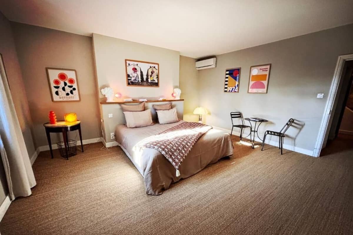 Ein Schlafzimmer mit einem Bett, Nachttischen, einem Sessel und Wandbildern.