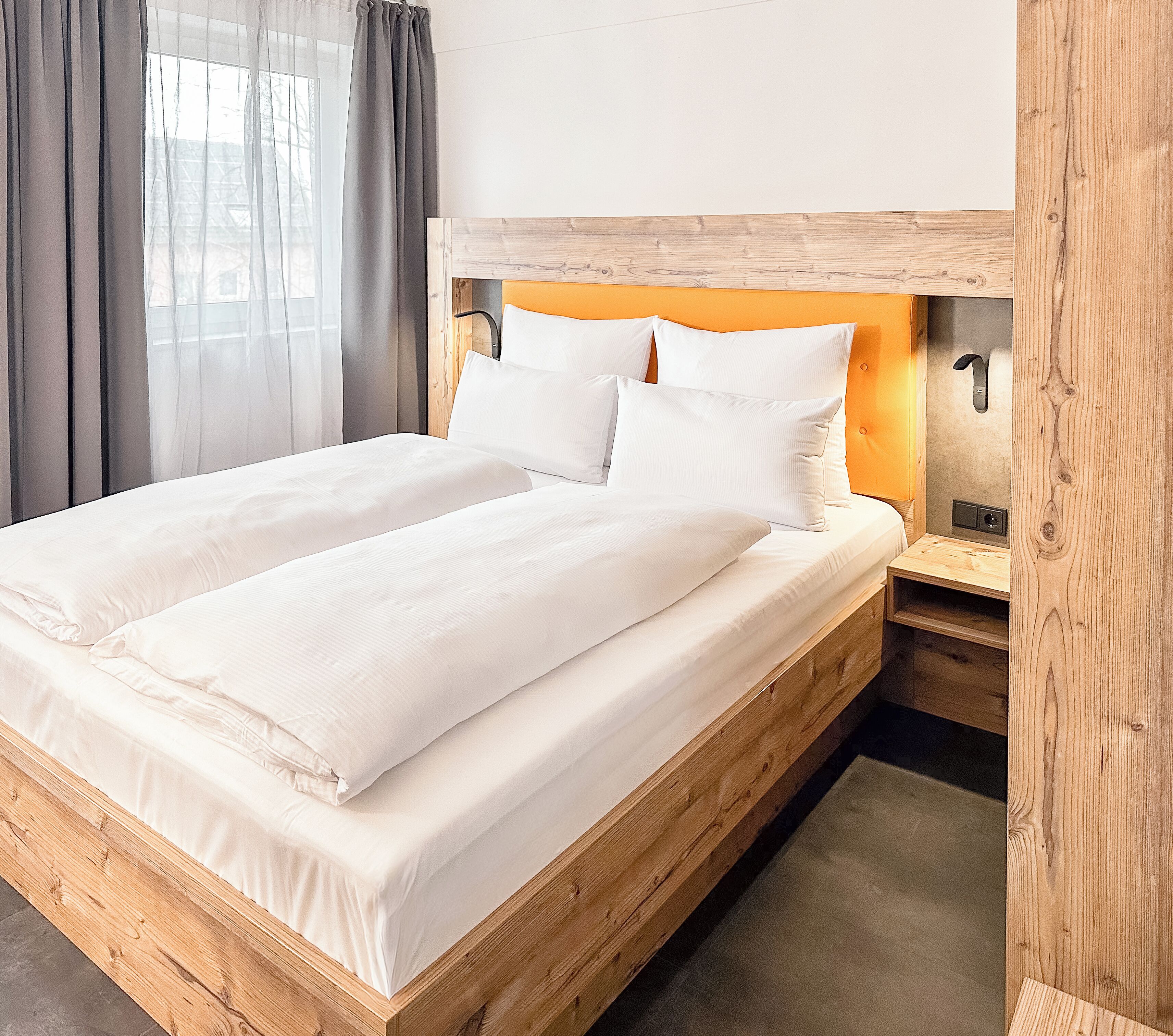 Una cama con estructura de madera, ropa de cama blanca y cabecera con lámpara.