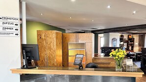 A hotel reception area with a marble counter, a wooden panel wall, and a sign indicating conference rooms. - THE GOOD ONE Hotel  (Landshut)