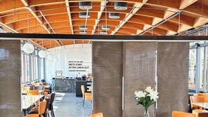 A modern dining area with round tables and orange chairs, a wooden ceiling, and a bar in the background. - THE GOOD ONE Hotel  (Landshut)