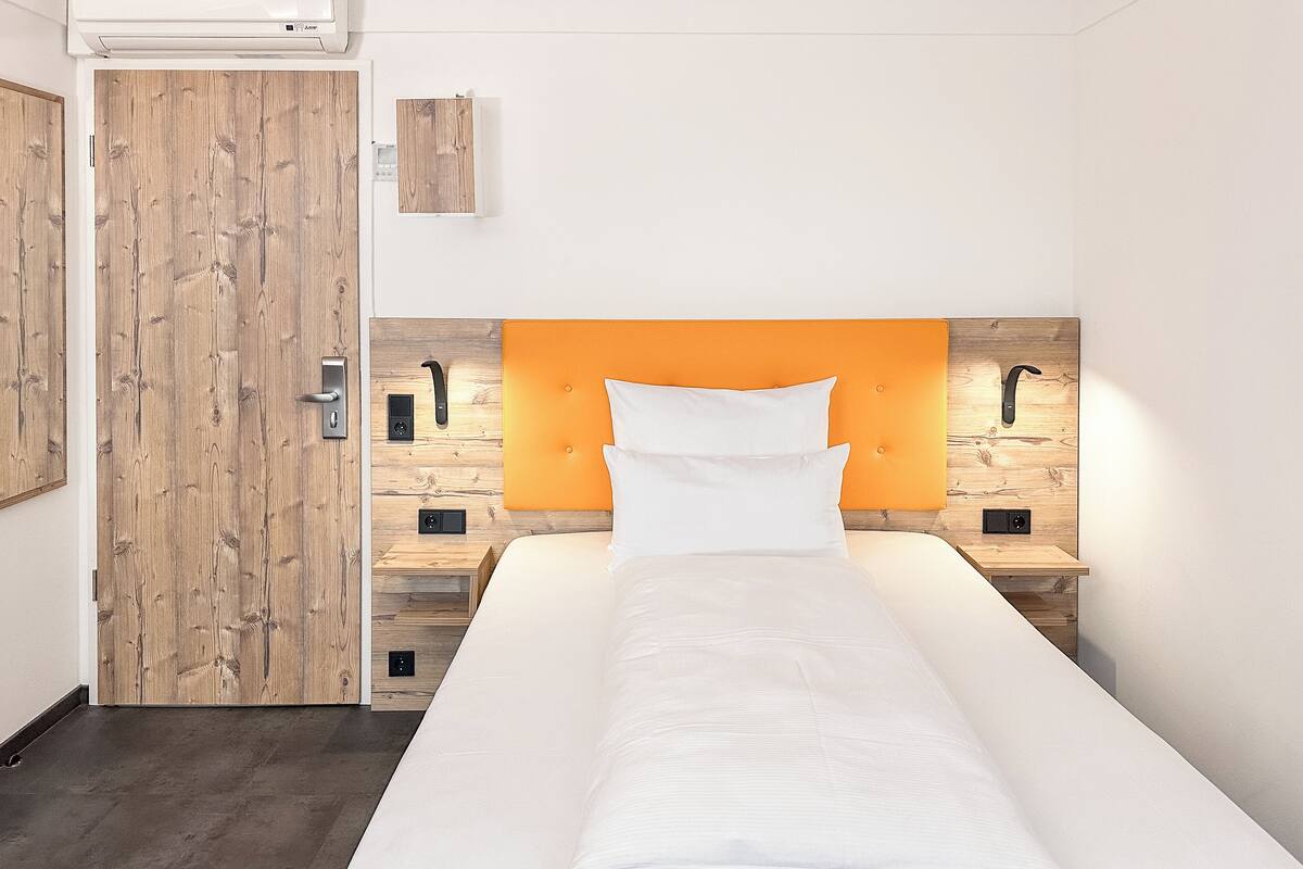 A single bed with a wooden headboard, a bedside table, and a nightstand.