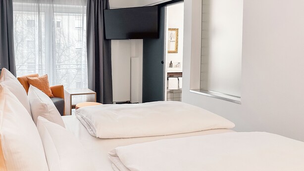 A hotel room with a neatly made bed, a television, a small table, and a window with curtains. - THE GOOD ONE Hotel  (Landshut)