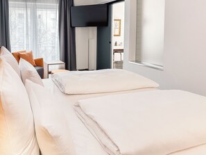 A hotel room with a neatly made bed, a television, a small table, and a window with curtains. - THE GOOD ONE Hotel  (Landshut)