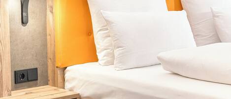 A modern bedroom with a wooden headboard, a bedside table, and a built-in outlet.