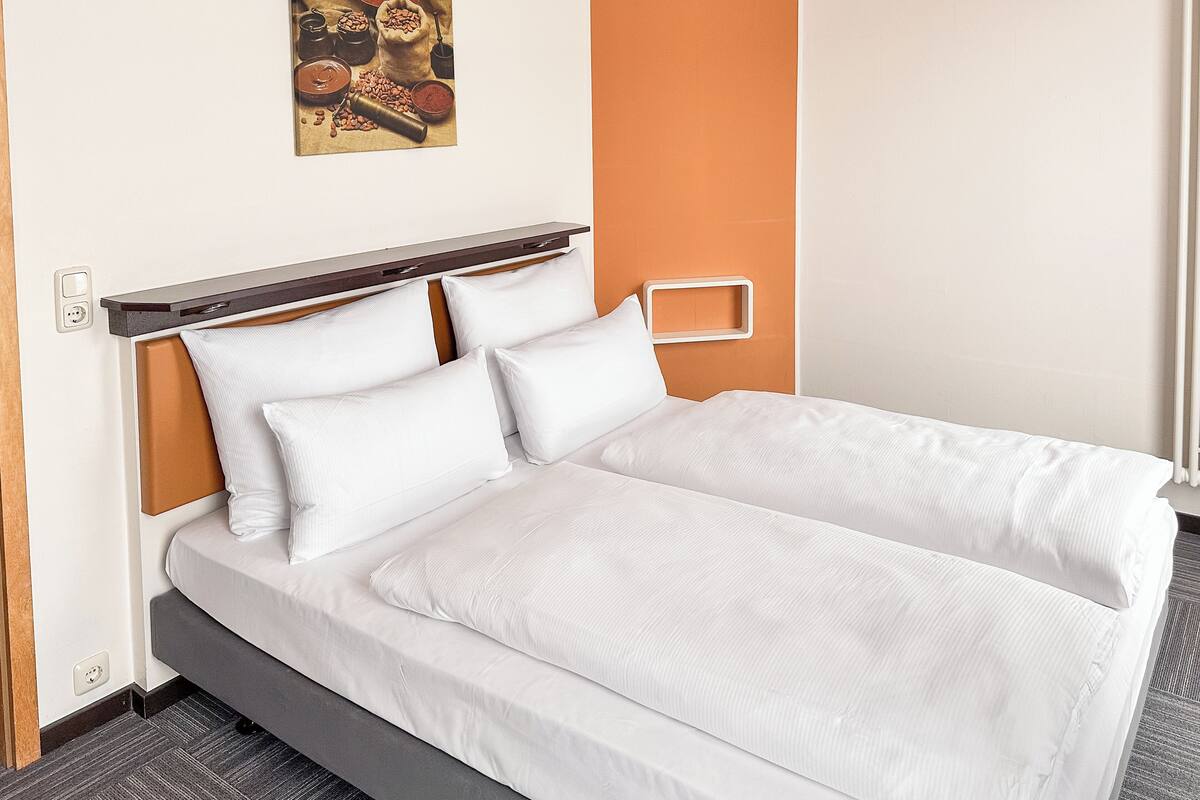 A neatly made bed with white linens, a wooden headboard, and a small picture frame on the wall.