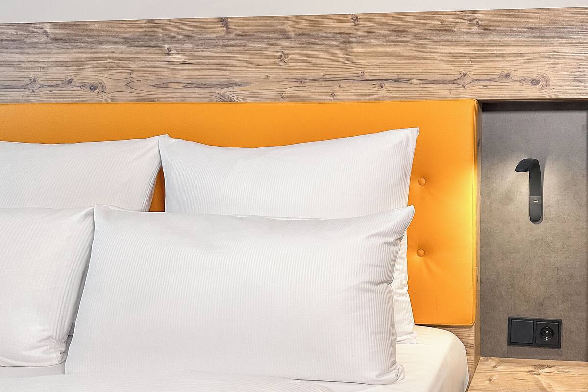 A neatly made bed with white linens and pillows, a wooden headboard, and a bedside table with a number '1' sign.