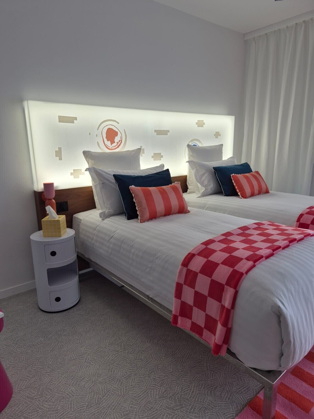 A hotel room with a bed, bedside tables, a wall-mounted headboard, and a bedside lamp.