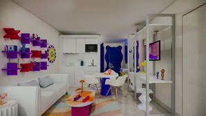 A modern living room with a white sofa, a coffee table, and a colorful rug. There are purple and red shelves with various items, a kitchen area with a microwave, and a blue curtain. - Symone Poitiers  (Poitiers)
