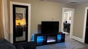 Un salón con un televisor de pantalla plana sobre un soporte negro, un sofá gris y una chimenea con luz azul.