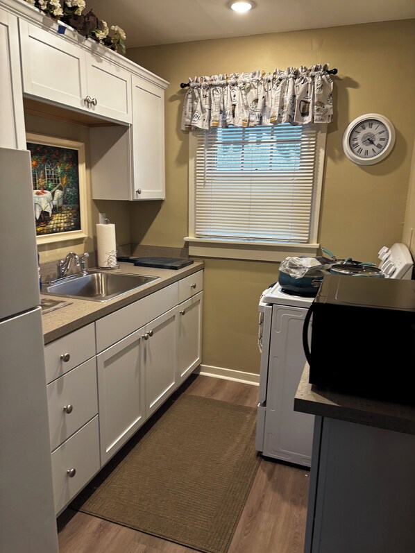 A compact kitchen with white cabinets, a sink, a microwave, and a clock on the wall.