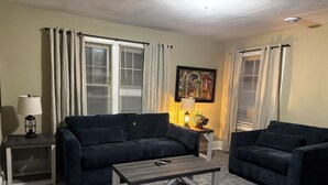 Una sala de estar con un sofá azul oscuro, un sillón a juego, una mesa de centro, una lámpara y un cuadro en la pared.