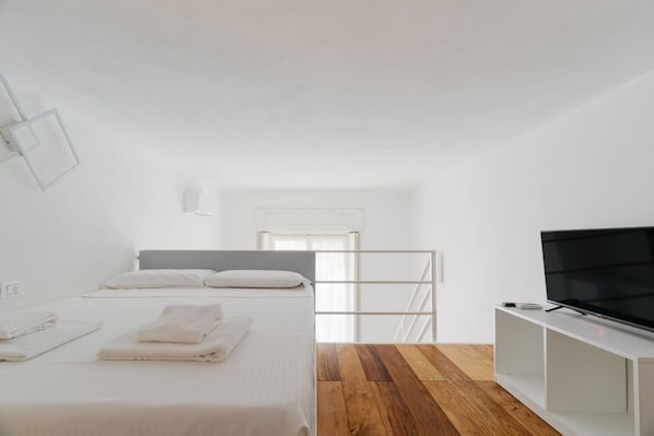 A bedroom with a bed, a TV, and a wooden floor. - GuestHost - Modern mezzanine studio apartment of 35 m2, ideal for two people, located on the raised ground floor of a typical Milanese building (stairs to access the apartment).The property is located a stone's throw from the M1 Lima stop in a strategi (Milan)