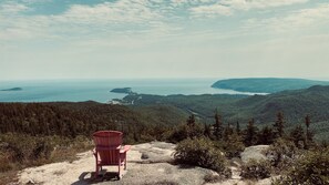 Una silla Adirondack roja sobre un promontorio rocoso con vistas a un paisaje costero con bosques densos y islas distantes.