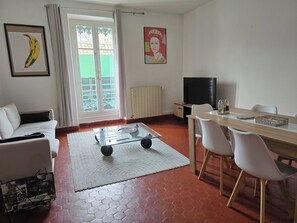 A living room with a sofa, a coffee table, a dining table with chairs, a TV, and a window with curtains. - 160m² Bright Flat in Central Nîmes (Nîmes)