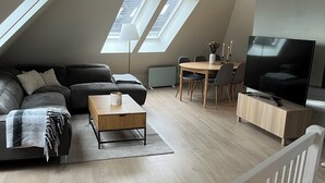 Moderni, avoimen pohjaratkaisun asunto, jossa on kalteva katto, kattovalokuvioita, suuri televisio, sohva, ruokapöytä ja pieni keittiöalue.