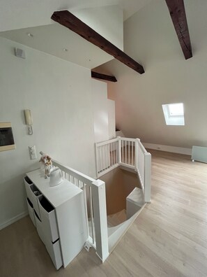Ein geräumiger Raum mit einer weißen Treppe, einem kleinen Tisch mit einer Dekoration und einem Fenster, das für natürliches Licht sorgt.