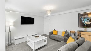 Ein modernes Wohnzimmer mit einem weißen Sofa, einem Couchtisch, einem Fernseher und einem gerahmten Poster an der Wand.