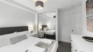 Ein modernes Hotelzimmer mit einem großen Bett, Nachttischen, einem Spiegel, einer weißen Kommode und einer Deckenleuchte.