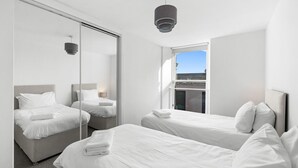 Habitación de hotel moderna con dos camas, un espejo grande y vistas de la ciudad a través de una ventana.