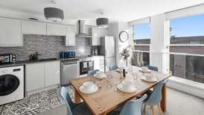 Una cocina moderna con armarios blancos, una mesa de comedor de madera para cuatro personas y un ventanal con vistas a la ciudad.