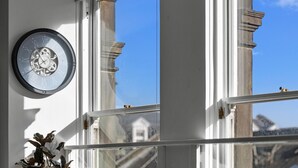 Una habitación con un reloj de pared grande, una ventana que ofrece vistas a edificios y una planta en el alféizar.