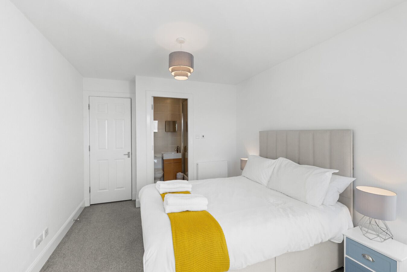 A hotel room with a bed, a nightstand, a lamp, and a bathroom visible through an open door.