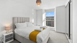 Un dormitorio moderno con cama, mesita de noche, lámpara y vistas al exterior.