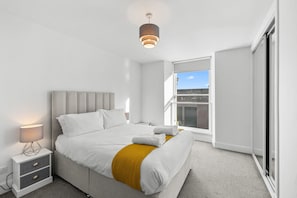 Une chambre à coucher moderne avec un lit, une table de chevet, une lampe et une vue sur l’extérieur.