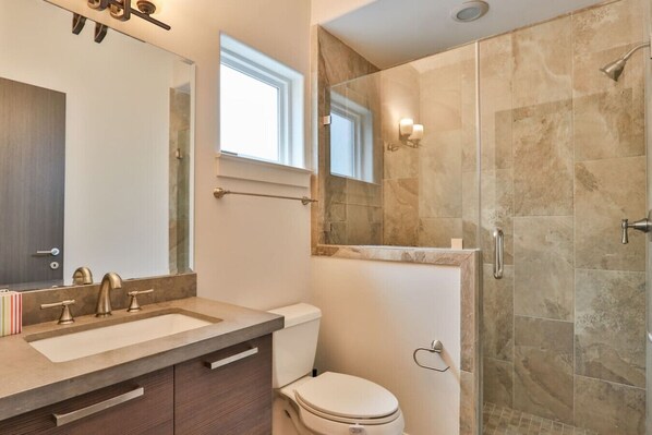 A bathroom with a large mirror, a sink, a toilet, and a shower area. - Montrose Art King Bed with Rooftop | Near Downtown (Houston)