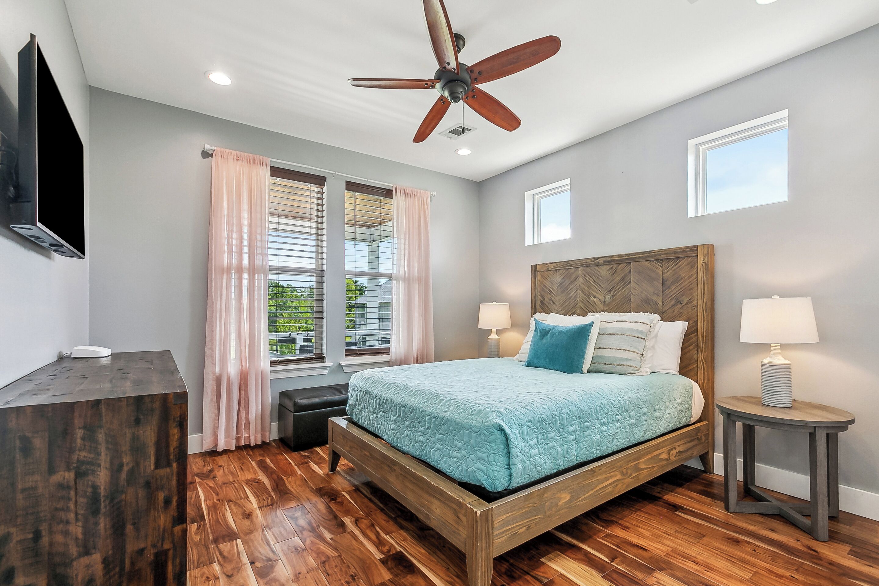 A bedroom with a wooden bed, a ceiling fan, a TV, and a window with curtains.
