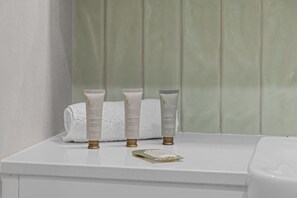 Three toiletry bottles on a white countertop with a green tiled wall in the background. - Quaint Townhouse in Bustling Locale (Brisbane)