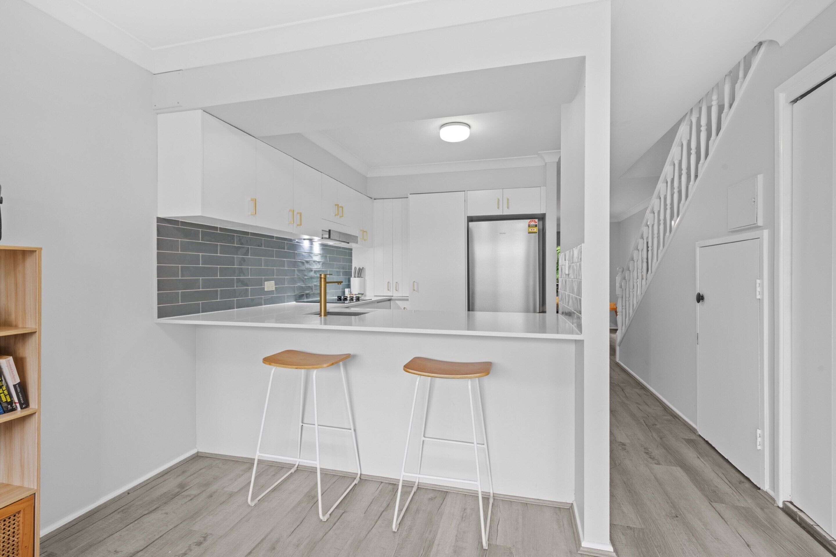 Una cocina moderna con armarios blancos, un refrigerador de acero inoxidable y dos taburetes de madera.