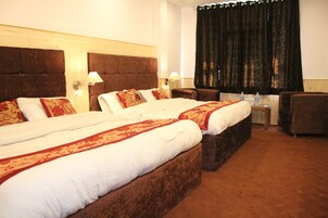 A hotel room with two large beds, a small table, a chair, and a large window with curtains.