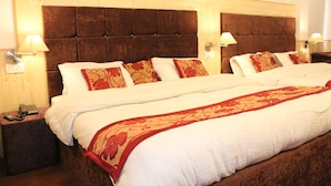 Un lit double avec une tête de lit marron, du linge de lit blanc et des coussins à motifs floraux rouges. Il y a des lampes de chevet de chaque côté du lit.
